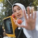 A woman in a hijab poses with a vintage red telephone outdoors.